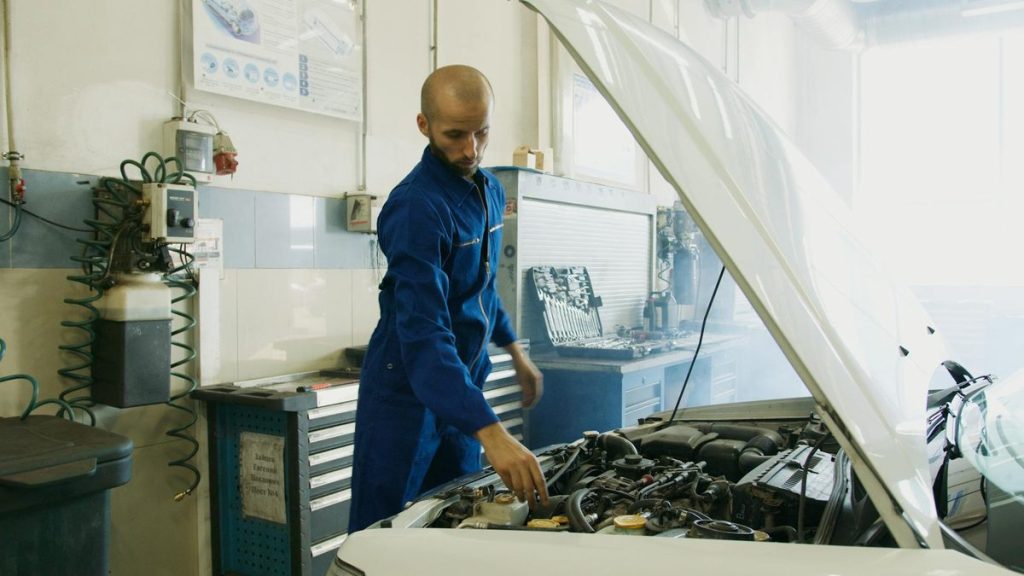 A professional mechanic carefully inspecting a car engine inside a well-equipped auto repair garage